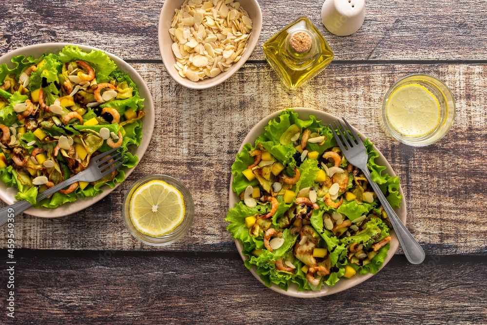 Delicious light dinner, lettuce with fried slices of zucchini, mango and shrimp and almond petals, water with lemon in a glass Delicious light dinner, lettuce with fried slices of zucchini, mango and shrimp and almond petals, water with lemon in a glass