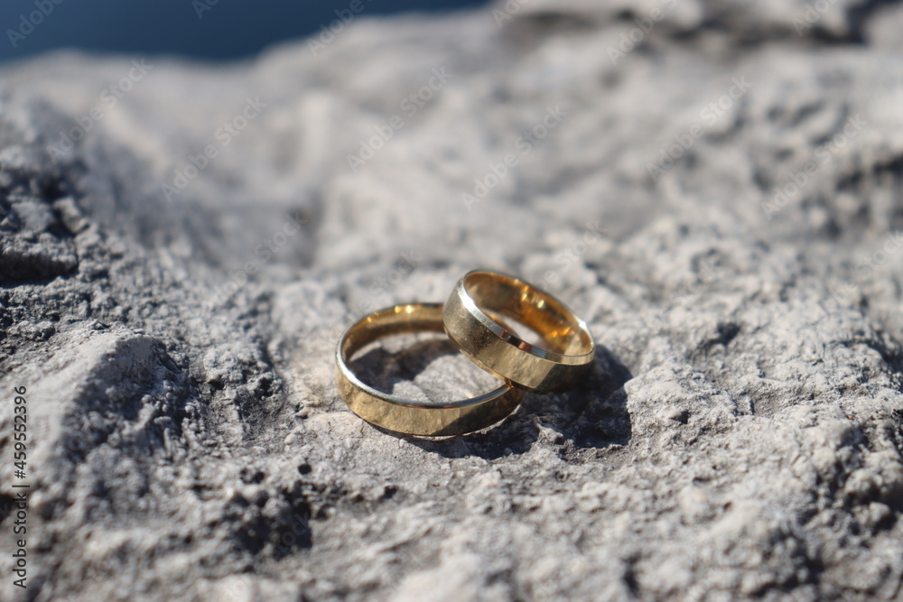 polished gold wedding rings for men and women lie on a stone surface. Against the background of the dark blue water of the lake