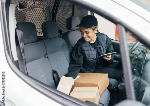 Smiling woman sitting on driver's seat checking packages and holding a digital tablet