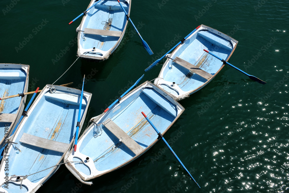A group of row boats lashed together seen from above, with the sun glistening off the water.