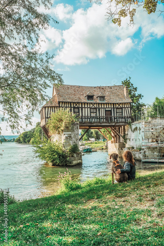 A Weimaraner breed dog next to a young girl sitting in front of the old mill on the medieval bridge in Vernon, Normandy