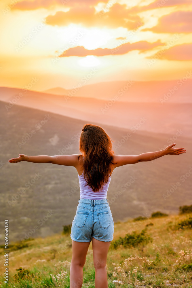 Rear view a young woman on the mountainside at sunset enjoying the view of the mountains. The concept of relaxation and peace. Rear view a young woman on the mountainside at sunset enjoying the view of the mountains. The concept of relaxation and peace.