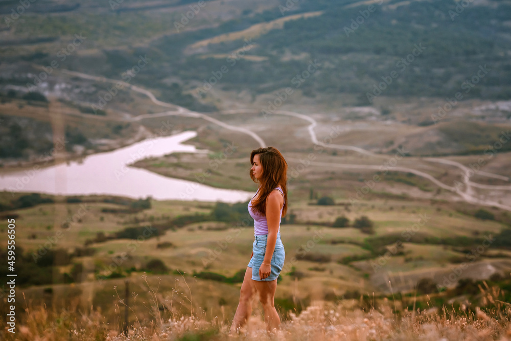 Naklejka premium Beautiful slender woman on top of a mountain at sunset. Amazing landscape with a gradient of mountains. The concept of sports and active life.
