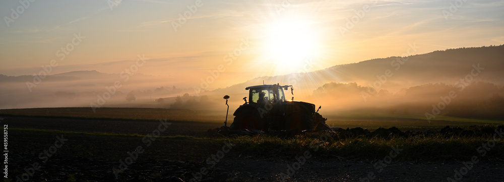 Tractor ploughing the field at sunrise in late summer or autumn. - obrazy, fototapety, plakaty 