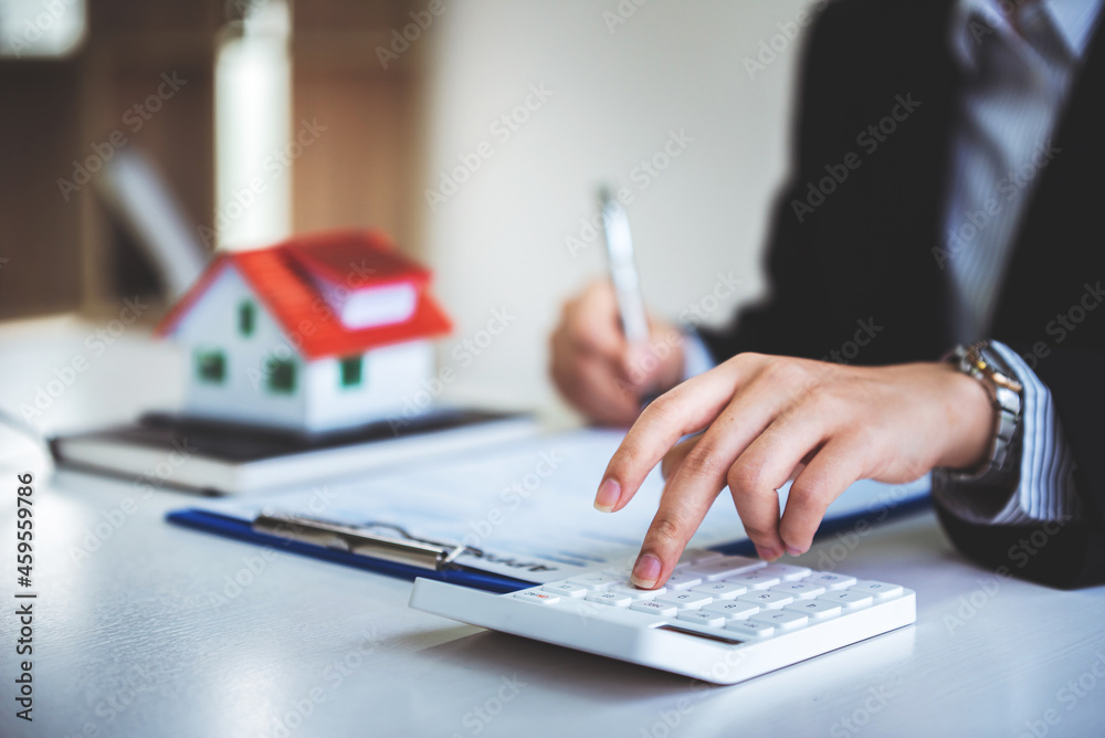 Fototapeta premium A young woman's hand presses a calculator to determine and summarize the cost of mortgage home loans for refinancing plans, lifestyle concepts.