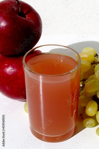 glass of juice and fruits apples and grape in the white background