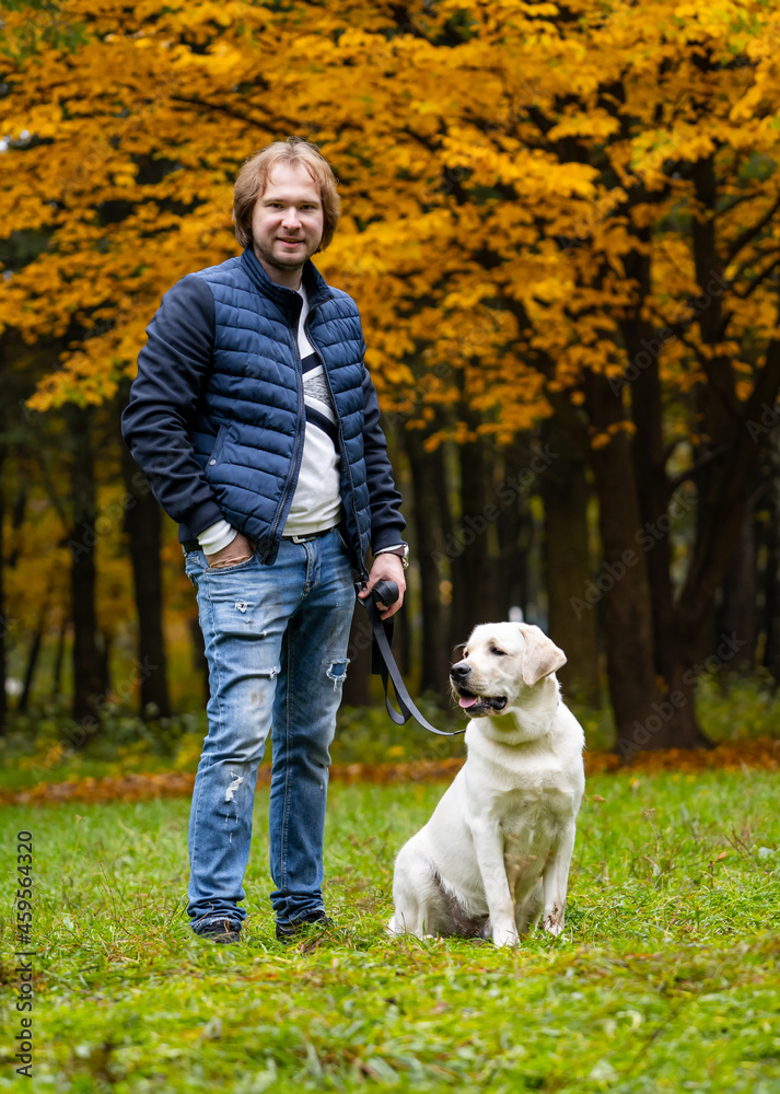 Man looks at camera while having a walk with retriver dog. Fabulous autumn park in golden colors. Full body portrait. Closeup Man looks at camera while having a walk with retriver dog. Fabulous autumn park in golden colors. Full body portrait. Closeup