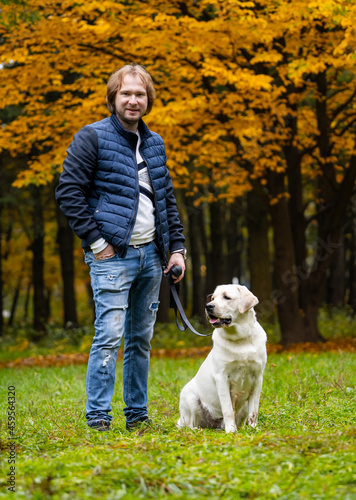 Man looks at camera while having a walk with retriver dog. Fabulous autumn park in golden colors. Full body portrait. Closeup