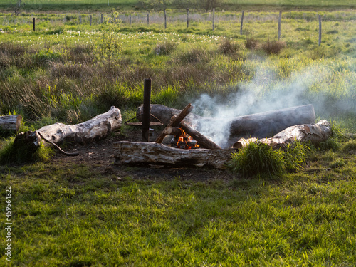 Campfire with logs and smoke at a campsite in field area with green grass.