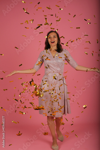 young happy beautiful slender girl in pink dress catches confetti dress pink background