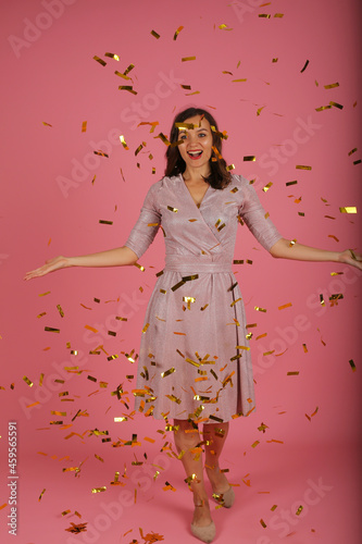 young happy beautiful slender girl in pink dress catches confetti dress pink background