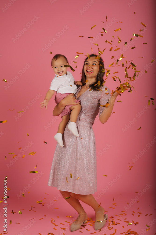 
a young mother in a pink dress holds her little son in her arms for a confetti party