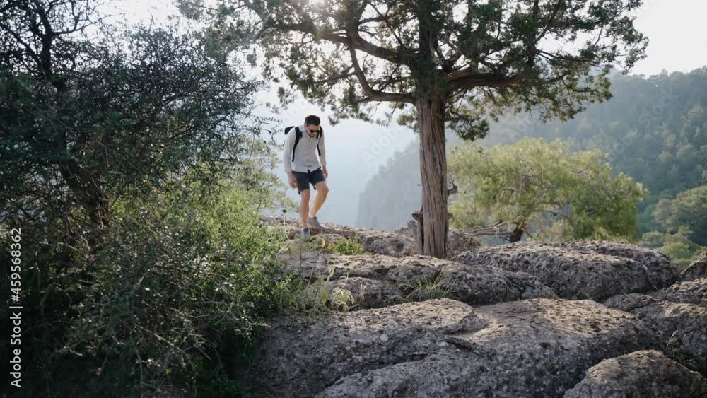 Guy traveler walks over the stones on the mountain, around the trees. The beautiful setting sun is shining. A magical landscape. High quality 4k footage Guy traveler walks over the stones on the mountain, around the trees. The beautiful setting sun is shining. A magical landscape. High quality 4k footage
