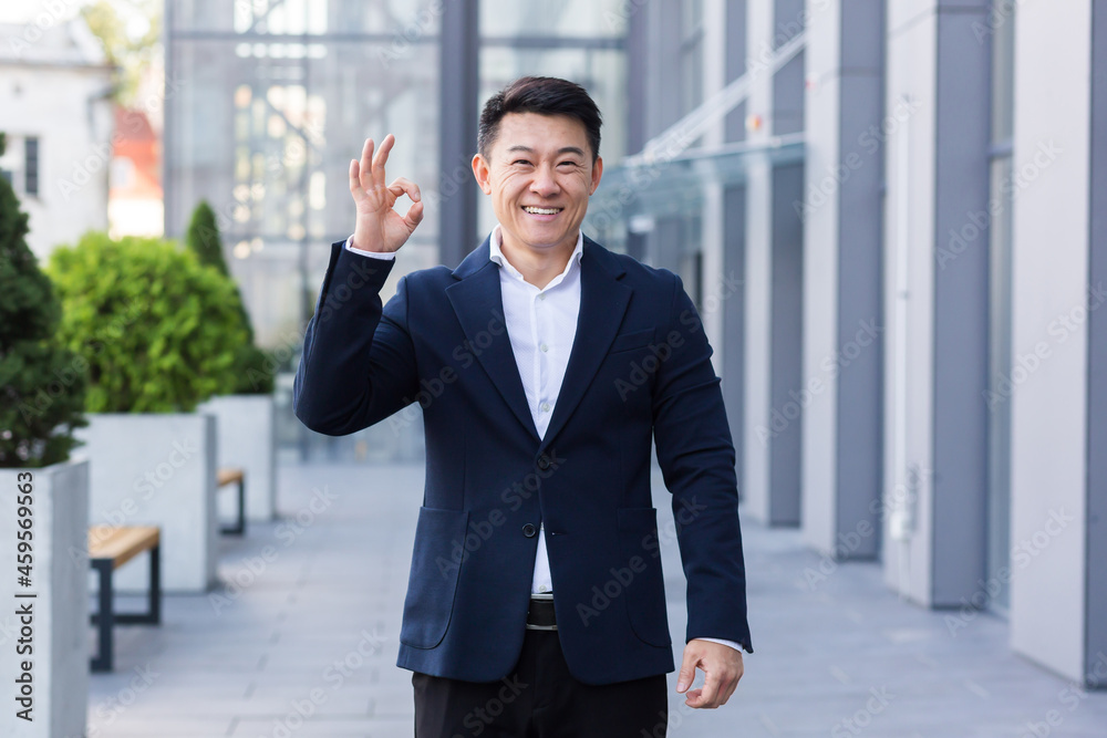 Male businessman salesman asian in business suit smiles and shows his hand all ok Male businessman salesman asian in business suit smiles and shows his hand all ok