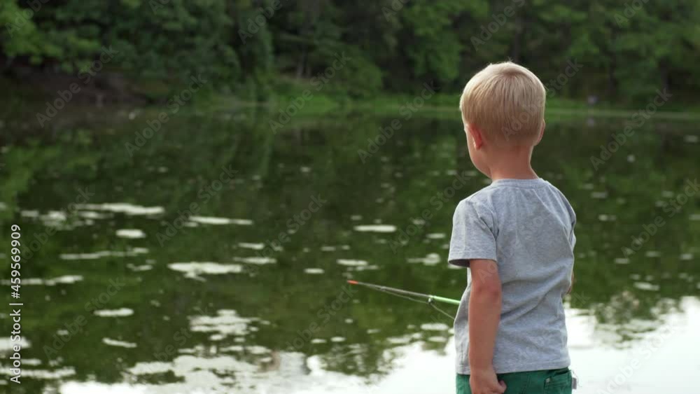 Back of a caucasian boy in t-shirt fishing at small pond in the park. A 4-years old boy with a fishing rod in calm summer evening. Back of a caucasian boy in t-shirt fishing at small pond in the park. A 4-years old boy with a fishing rod in calm summer evening.