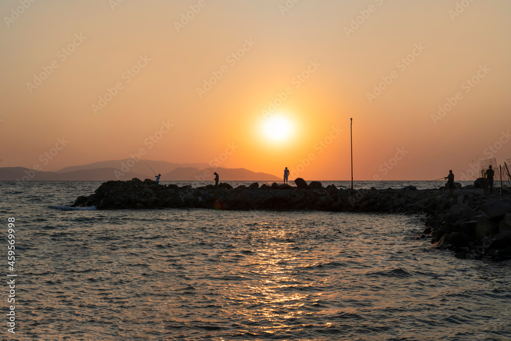 A stony pier and waves in the sea at sunset with fishers, Sevgi Beach, Kusadasi, Aydin, Turkey