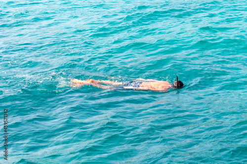 Unrecognizable man with mask snorkeling in clear turquoise water at tropical sea. Back and top view
