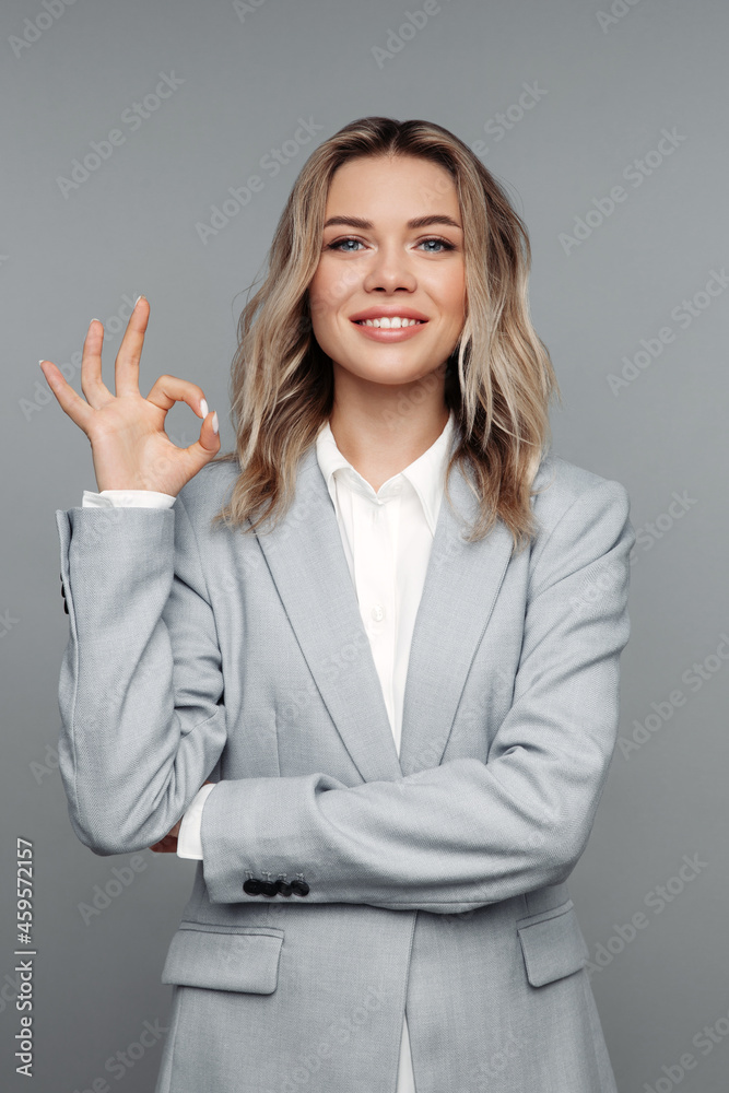 Satisfied customer showing ok sign happy smiling. Young confident businesswoman in gray suit hold okay finger gesture for service or client approval and satisfaction concept isolated over studio wall Satisfied customer showing ok sign happy smiling. Young confident businesswoman in gray suit hold okay finger gesture for service or client approval and satisfaction concept isolated over studio wall