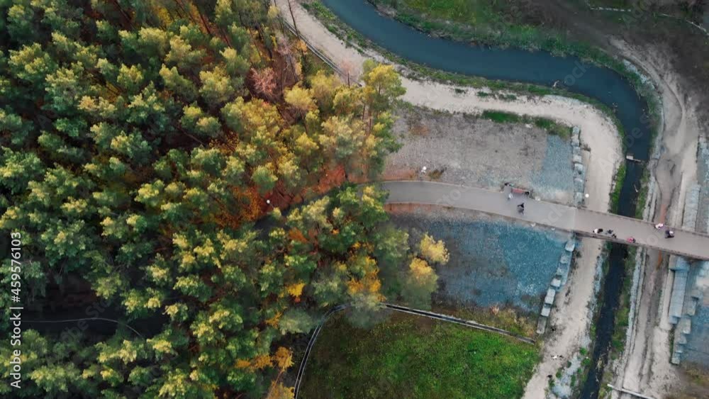 A drone flies over an autumn park with colorful autumn foliage, people walk across a bridge across a beautiful river on a walk in the park. A drone flies over an autumn park with colorful autumn foliage, people walk across a bridge across a beautiful river on a walk in the park.