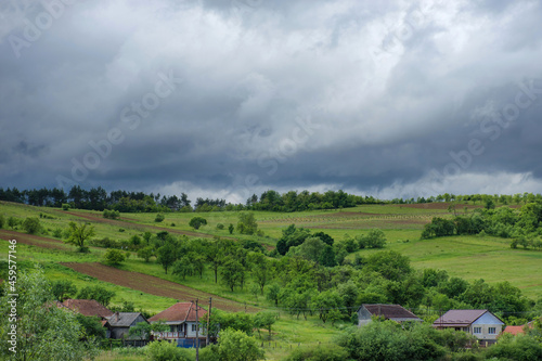 Landscape with charming little houses, agricultural fields and dramatic sky in Transylvania countryside, Romania