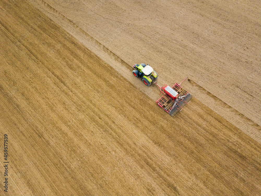 Aerial shot of a farmer seeding, sowing crops at field. Sowing is the process of planting seeds in the ground as part of the autumn time agricultural activities.
