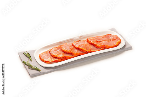lomo de cerdo adobado fresco cortado en filetes sobre bandeja blanca con pimenton en bol blanco decorativo, sobre servilleta de tela marron. aislada fondo blanco photo