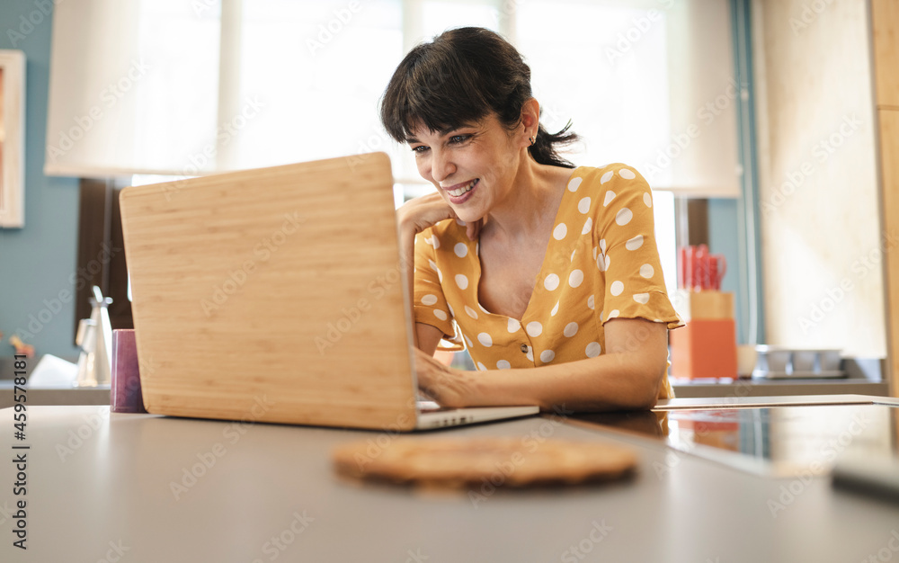 Happy mature woman using laptop on kitchen island at home Happy mature woman using laptop on kitchen island at home