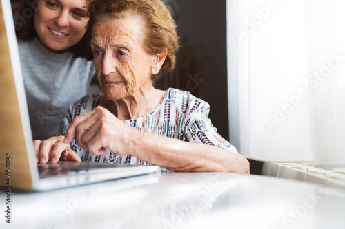 Smiling young woman assisting grandmother using laptop at home photo