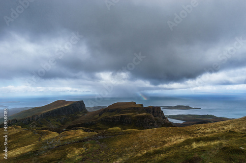 View over rocky landscape of landslide Quiraing on a dark rainy autumn day with rainbow, Isle of Skye, Scotland