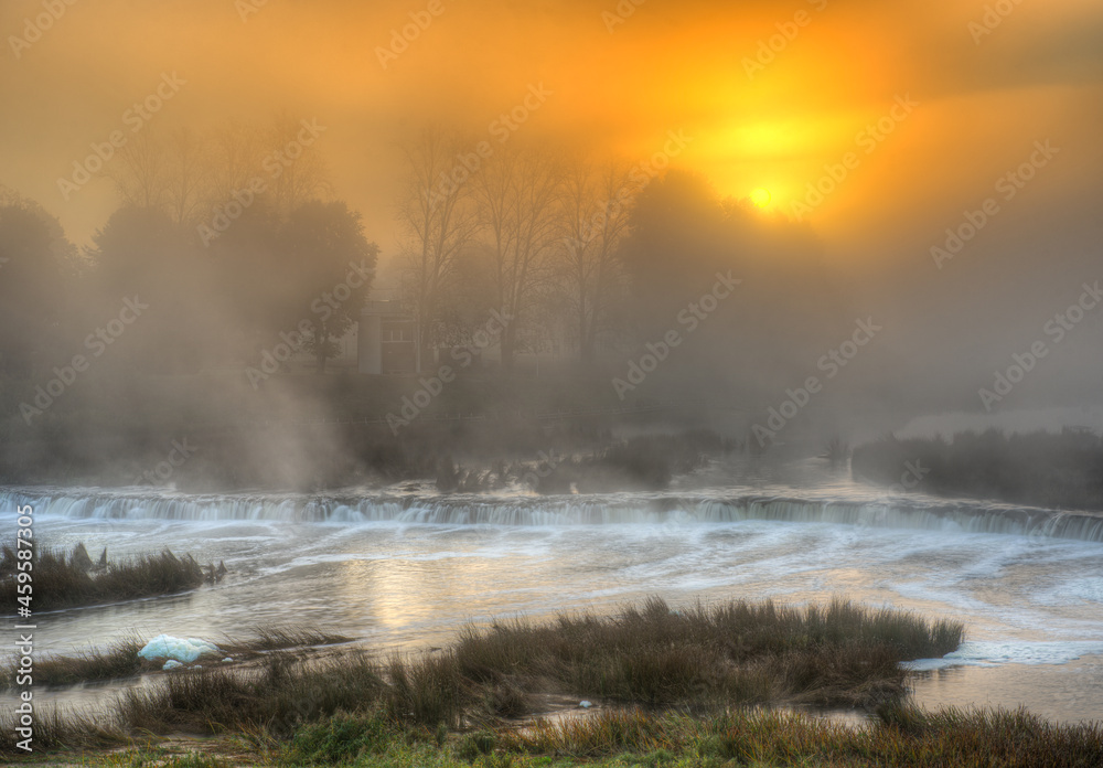 Beautiful sunrise in autumn morning. River Venta waterfall in the fog, Kuldiga, Latvia.