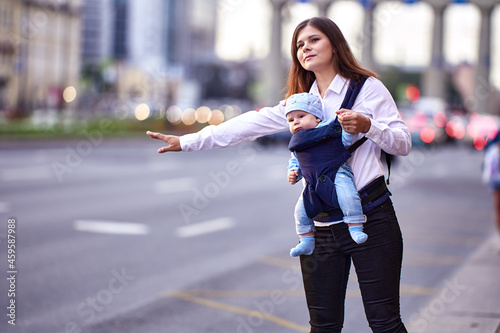 Woman with child in baby carrier is stopping taxi. © grigvovan