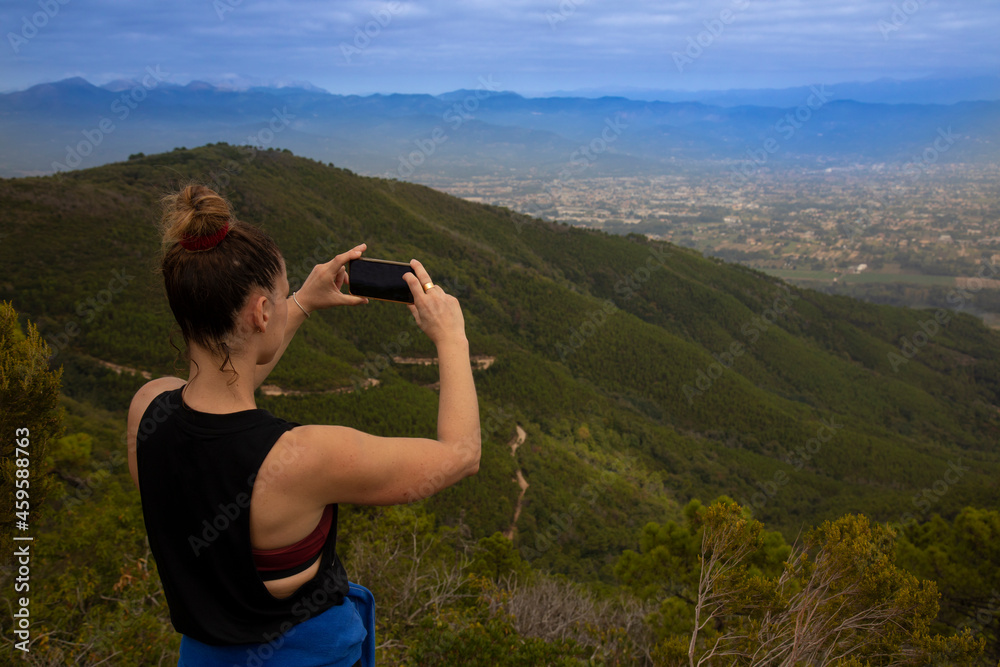 young athletic woman on the top of the mountain taking pictures of the panorama with her mobile phone