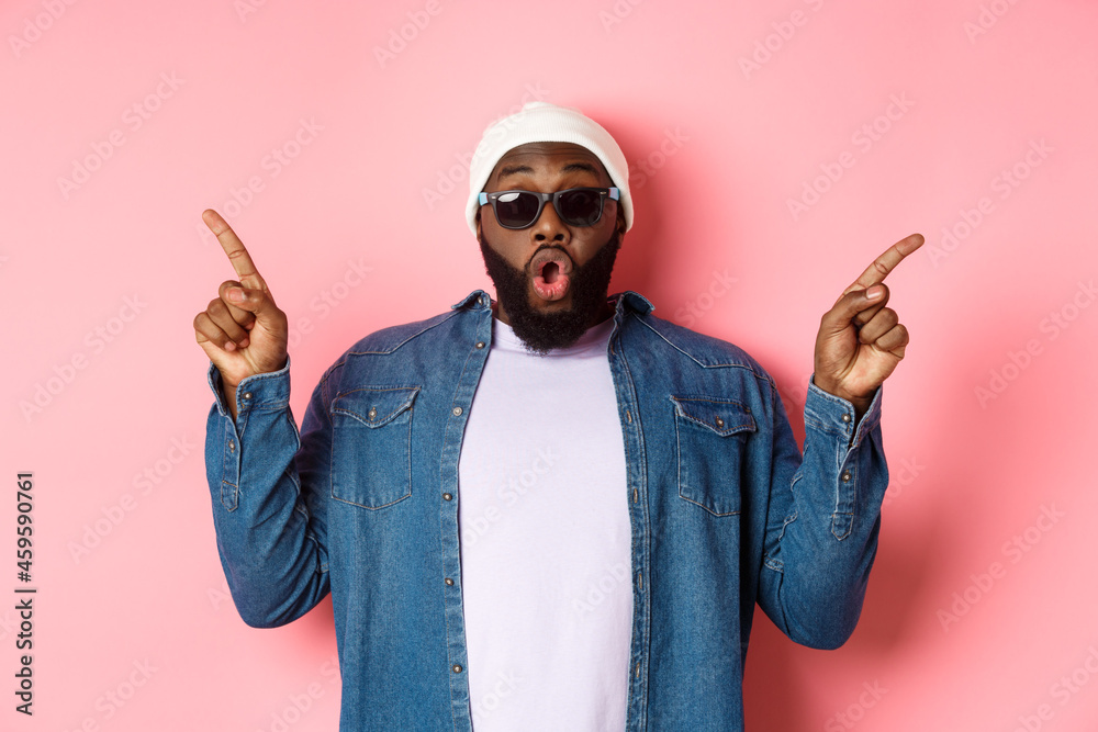 Amazed cool Black guy showing two variants, pointing fingers sideways ...