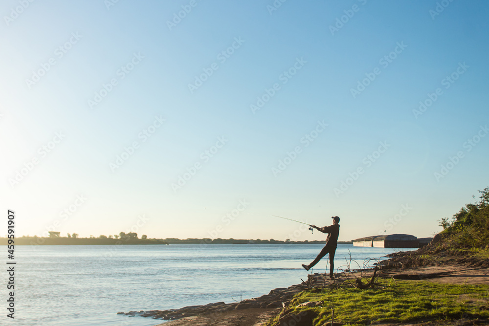 Man casting his fishing rod at the edge of the river.