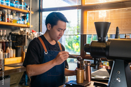Asian man barista using coffee grinder machine grinding roasted coffee beans at cafe. Male coffee shop owner brewing black coffee serving to customer. Small business restaurant food and drink concept