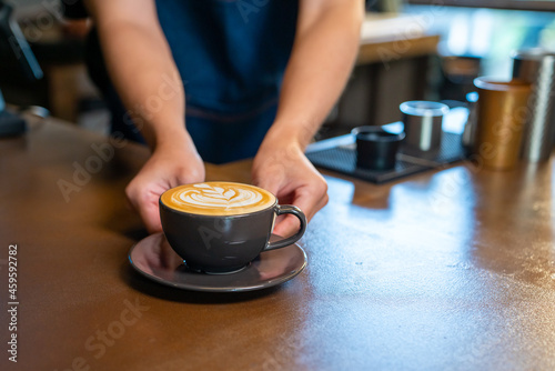 Asian man barista making hot coffee latte in coffee cup to customer on bar counter at cafe. Male coffee shop waiter serving hot coffee with milk to client. Small business restaurant owner concept.