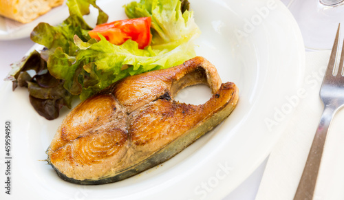 Tasty broiled steak of bonito served with vegetable salad on white plate..