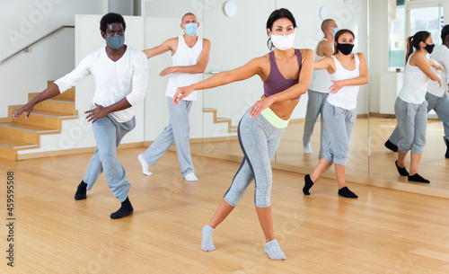 Group of people in protective masks practicing active rhythmic dancing in dance studio. Forced precautions in COVID pandemic