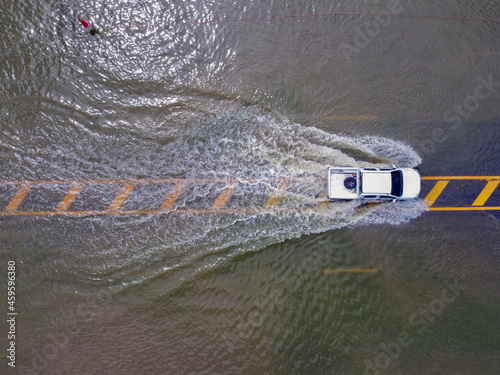 Flooded roads, people with cars running through. Aerial drone photography shows streets flooding and people's cars passing by, splashing water.