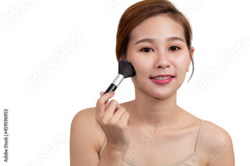 Close up portrait pretty Asian woman with cosmetic brush applying dry cosmetic tonal foundation on her face and looking at camera and smiling isolated on a white background. Fashion, beauty concept.