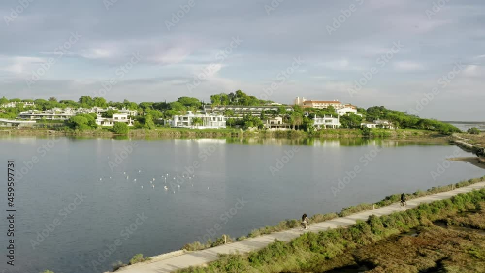 Panoramic view of picturesque landscape of houses around Quinta do Lago, Algarve, Portugal. Drone shot of people walking on path around lake. Flock of birds resting on water of pond, 4k footage Panoramic view of picturesque landscape of houses around Quinta do Lago, Algarve, Portugal. Drone shot of people walking on path around lake. Flock of birds resting on water of pond, 4k footage