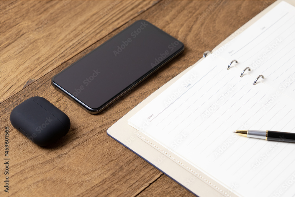 Open diary on wooden table with smart phone, head phone wireless and pen on book Open diary on wooden table with smart phone, head phone wireless and pen on book