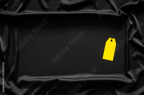 A yellow blank price tag on black smooth and wavy cloth with space for text. Black Friday concept.