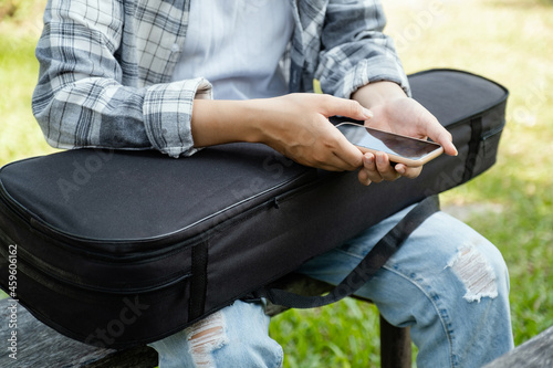A young woman violinist hand holding a smartphone and a violin sit waiting for an online class on a wooden chair