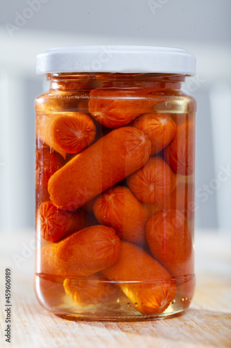 Photography Closed jar with canned mini sausages on wooden table