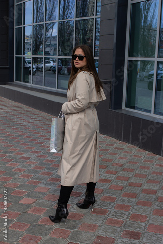 young brown-haired beautiful girl with green eyes and a light trench with shopping on the background of the city