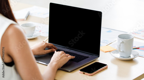 Close up shot of black blank screen monitor laptop notebook computer on working table with paperwork documents while unidentified unrecognizable female professional secretary typing on keyboard