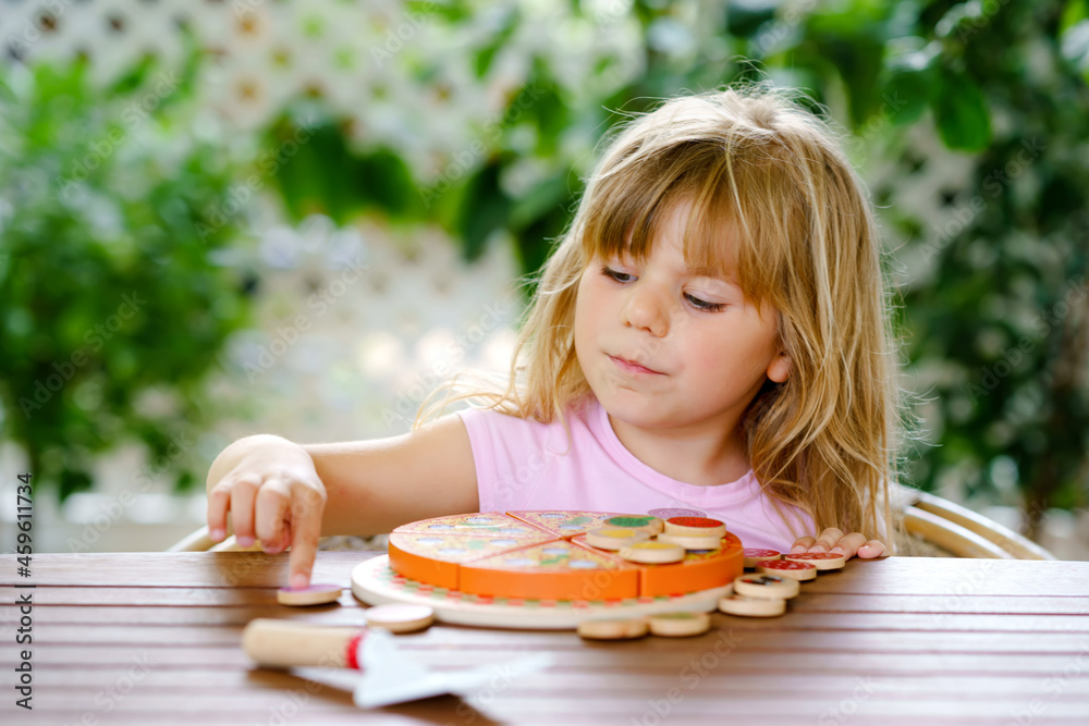 Little cute girl playing with wooden toy pizza. Preschool child having fun with children activity like, play with food, indoors. Little cute girl playing with wooden toy pizza. Preschool child having fun with children activity like, play with food, indoors.