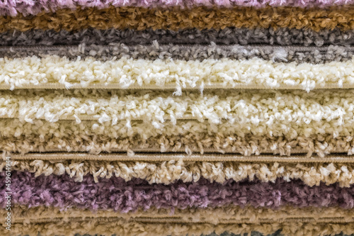 The texture of several multi-colored rolled-up carpets with a long pile. Side view, background.