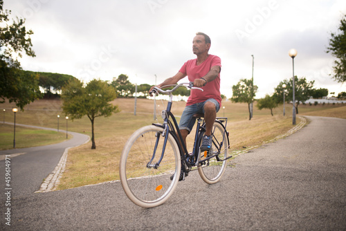 Confident mature man riding bike along park road. Portrait of active senior man on bicycle. Active seniors concept